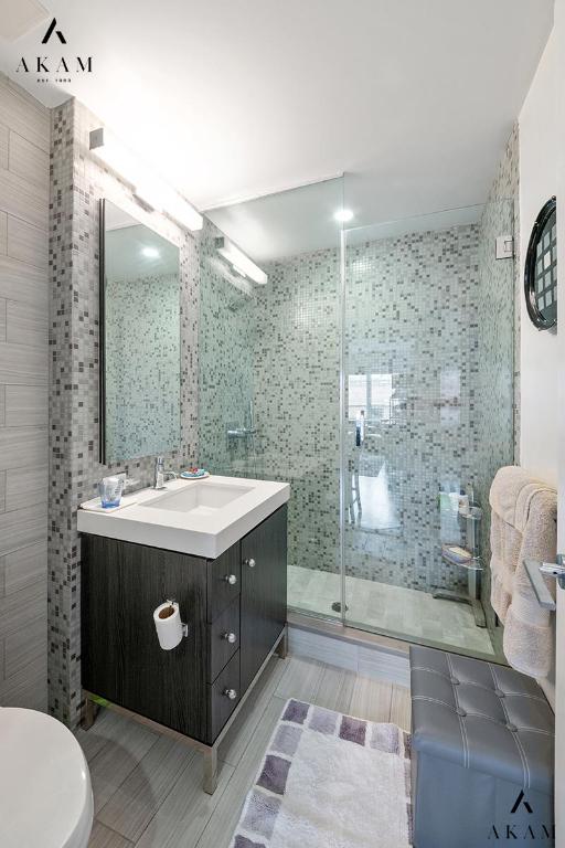 bathroom with vanity, a shower with door, tile walls, and toilet