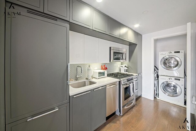 kitchen with gray cabinetry, stainless steel appliances, stacked washing maching and dryer, and backsplash