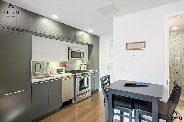 kitchen featuring stacked washer and dryer, sink, appliances with stainless steel finishes, gray cabinets, and backsplash