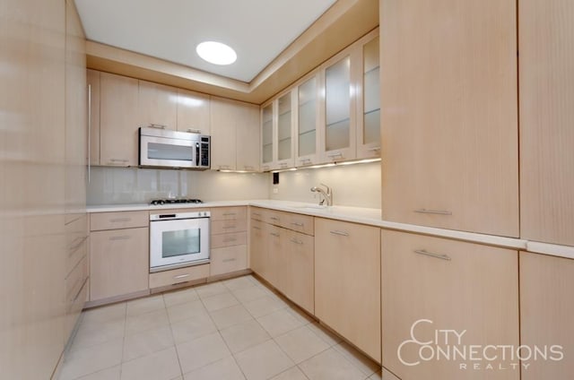 kitchen with white appliances, glass insert cabinets, light countertops, and light brown cabinetry