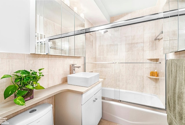 full bathroom featuring vanity, toilet, combined bath / shower with glass door, and tile walls