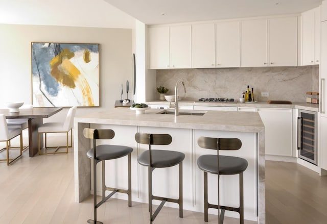 kitchen with a sink, wine cooler, light wood-style floors, white cabinetry, and tasteful backsplash