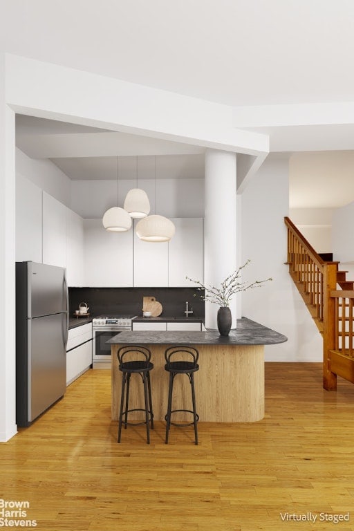 kitchen featuring white cabinetry, decorative light fixtures, a breakfast bar, stainless steel fridge, and gas range oven