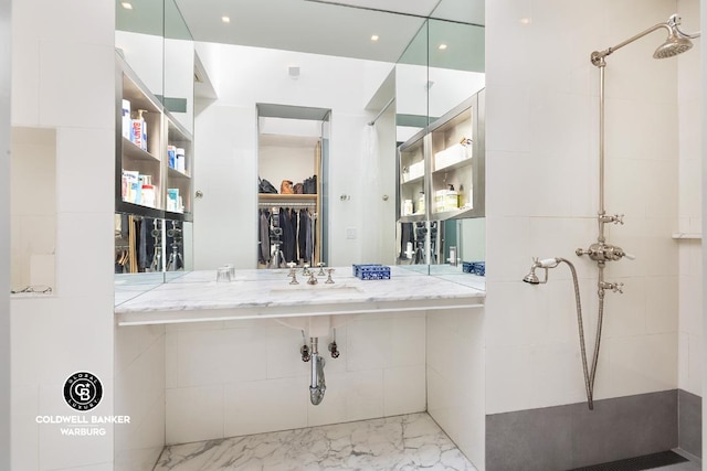 bathroom featuring a walk in closet, a tile shower, and a sink