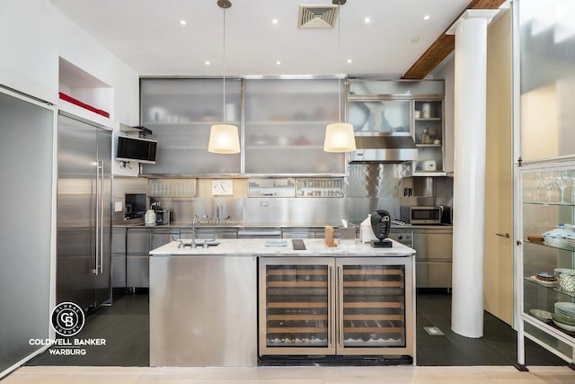 kitchen featuring wine cooler, backsplash, hanging light fixtures, light stone countertops, and a center island with sink