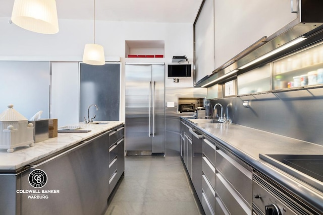 kitchen with built in refrigerator, a sink, white cabinets, hanging light fixtures, and modern cabinets