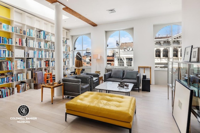 sitting room with light wood-type flooring, visible vents, and beamed ceiling