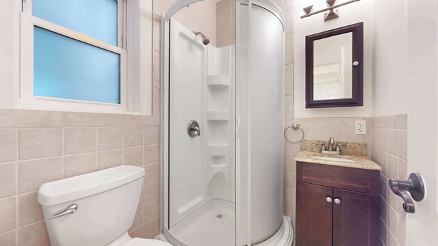 563 W 182nd St, New York City, NY 10033 - bathroom featuring tile walls, a shower stall, vanity, toilet, and wainscoting