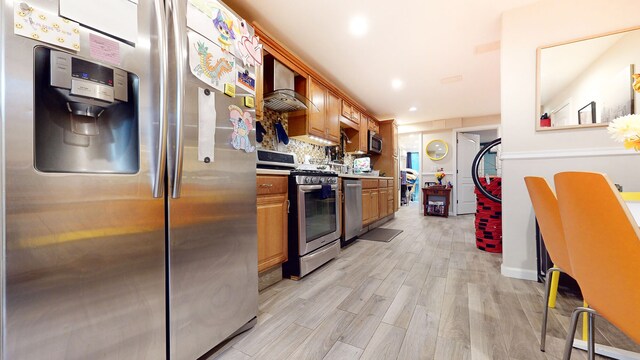 563 W 182nd St, New York City, NY 10033 - kitchen with stainless steel appliances, wall chimney exhaust hood, light wood finished floors, brown cabinets, and recessed lighting