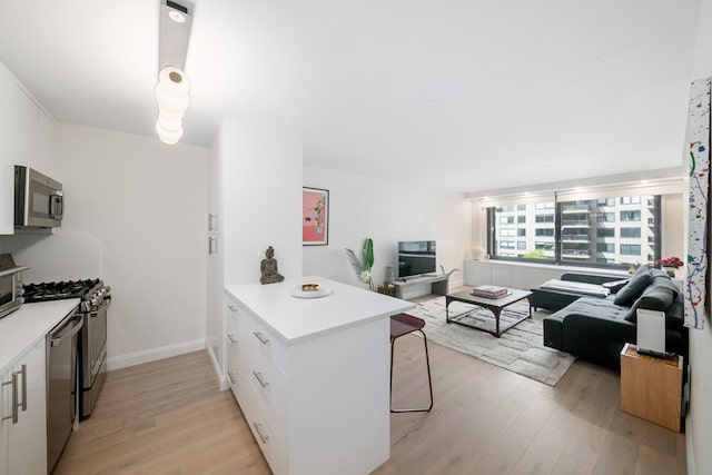 kitchen featuring stainless steel appliances, kitchen peninsula, white cabinets, and light wood-type flooring