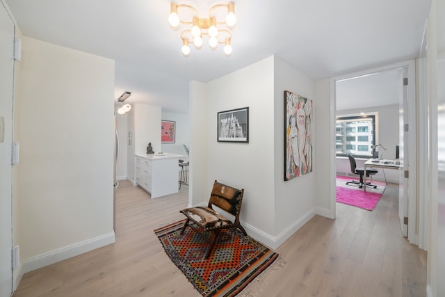 hall with light wood-style floors, baseboards, and a chandelier