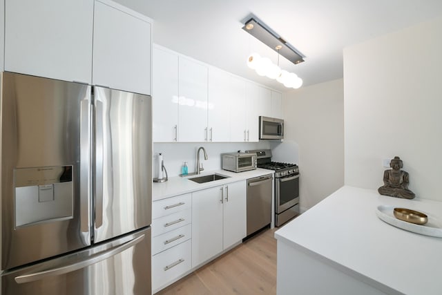 kitchen featuring white cabinets, stainless steel appliances, light countertops, light wood-style floors, and a sink