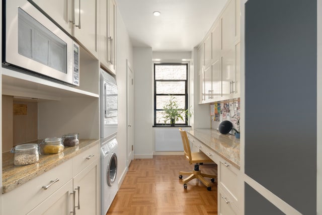 laundry room with cabinets, light parquet floors, and stacked washer / drying machine