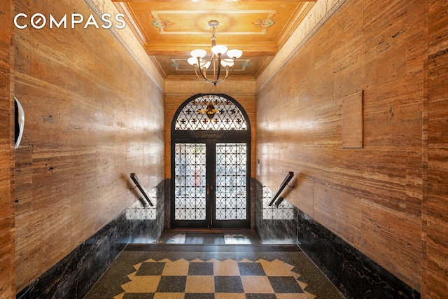 foyer entrance with an inviting chandelier, wood walls, crown molding, and french doors