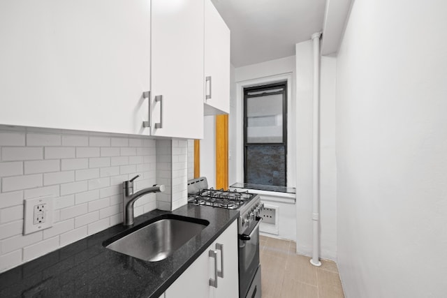 kitchen featuring sink, stainless steel gas stove, dark stone counters, decorative backsplash, and white cabinets