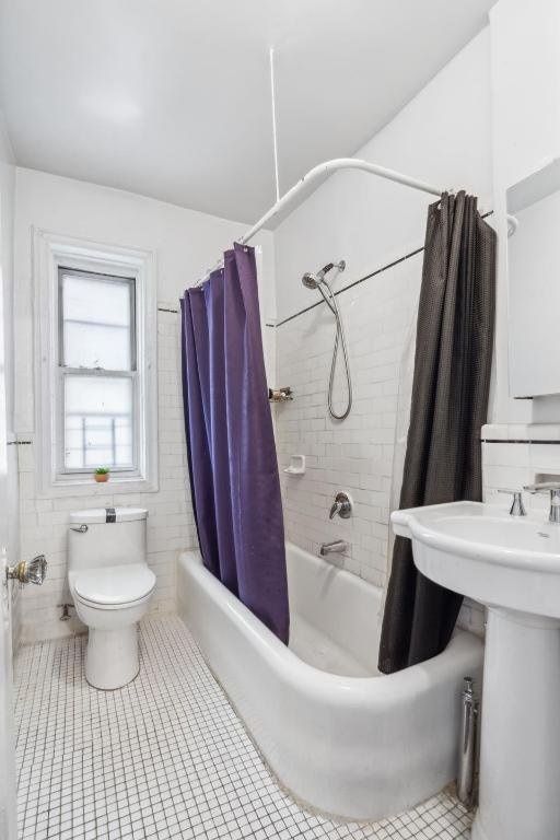 bathroom featuring tile patterned flooring, shower / tub combo, toilet, and tile walls