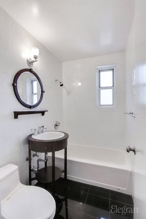 bathroom with toilet, tiled shower / bath combo, tile walls, and tile patterned floors