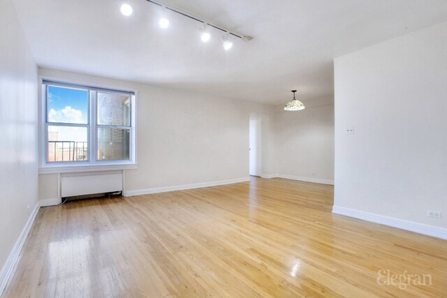 empty room with radiator, light wood-style floors, and baseboards