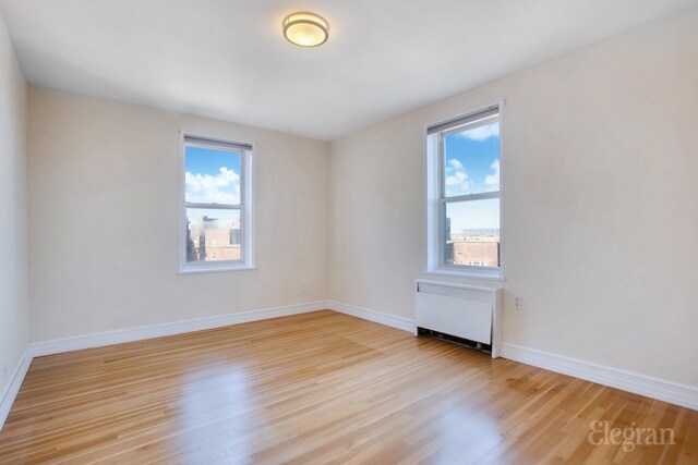 spare room featuring radiator heating unit, baseboards, and light wood-style flooring