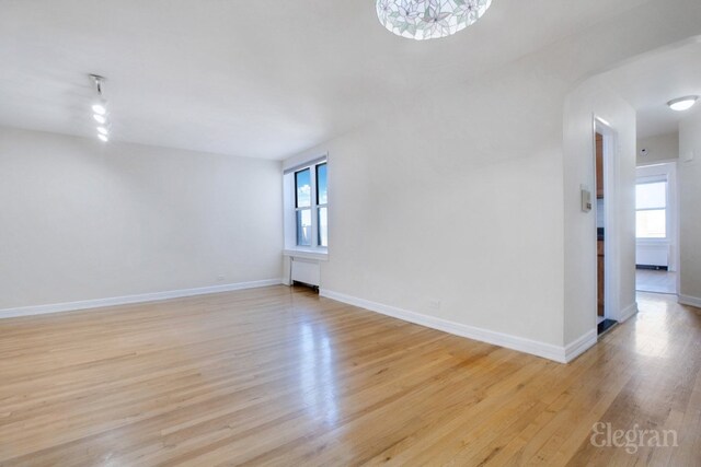 spare room with light wood-type flooring, a healthy amount of sunlight, and radiator heating unit