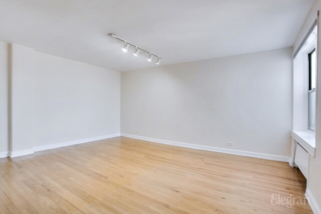 unfurnished room with rail lighting, light wood-style flooring, and baseboards