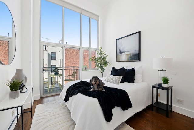 bedroom with baseboards, dark wood-type flooring, a towering ceiling, and access to exterior