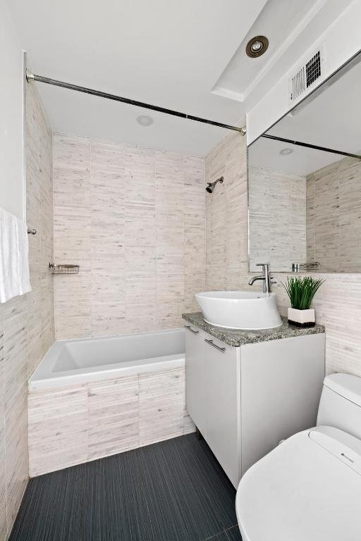 full bathroom featuring visible vents, toilet, tiled shower / bath, vanity, and tile walls