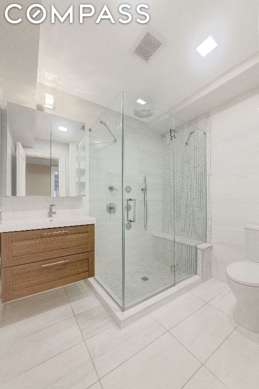 bathroom featuring toilet, tile patterned floors, vanity, and a shower with shower door