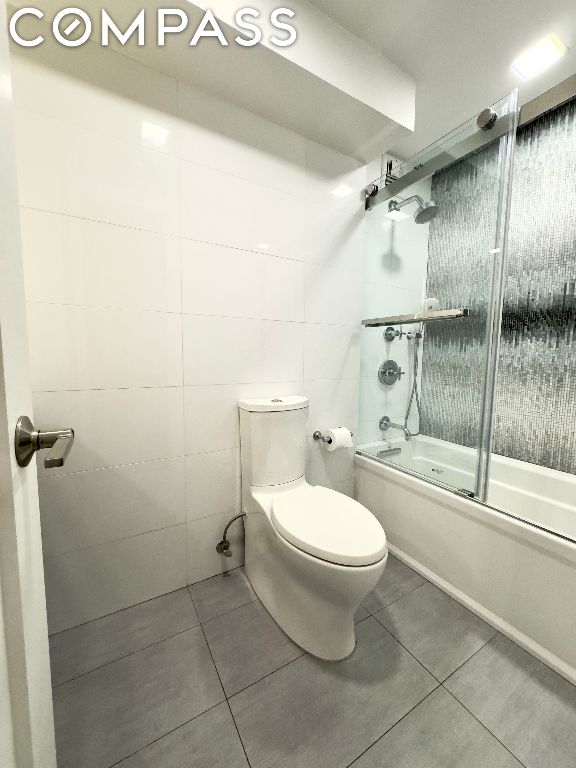 bathroom featuring toilet, tile patterned flooring, and enclosed tub / shower combo