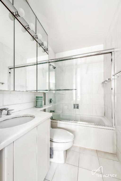 full bathroom featuring toilet, enclosed tub / shower combo, tile patterned flooring, tile walls, and vanity