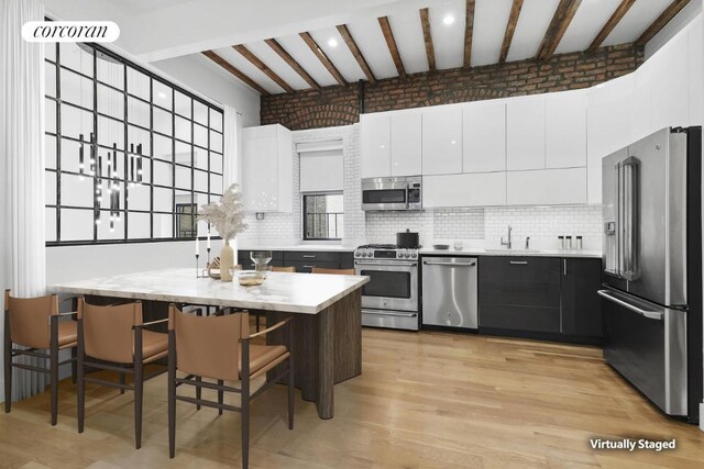 kitchen featuring sink, appliances with stainless steel finishes, white cabinets, beamed ceiling, and light wood-type flooring