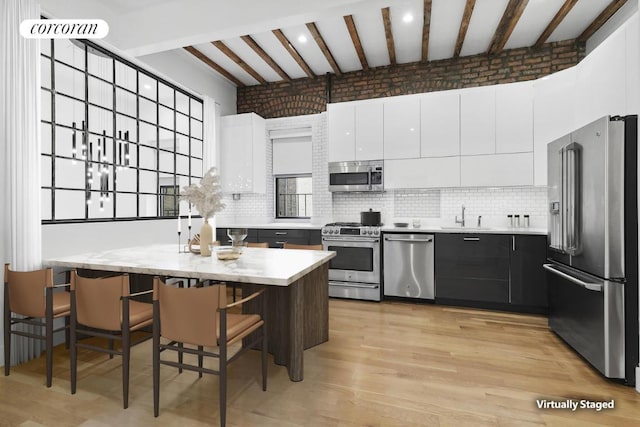 kitchen with white cabinets, a sink, beam ceiling, stainless steel appliances, and backsplash