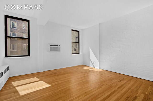 bedroom with radiator, cooling unit, brick wall, and hardwood / wood-style flooring