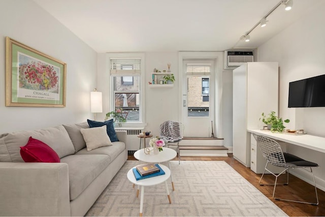 living room featuring hardwood / wood-style floors, radiator heating unit, built in desk, rail lighting, and a wall mounted AC