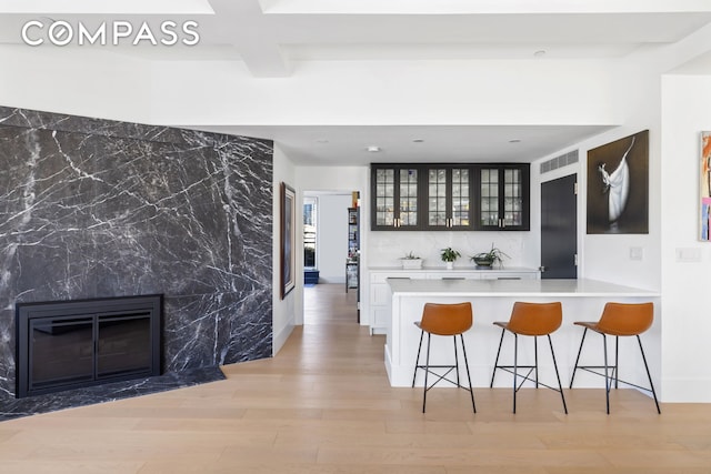 kitchen featuring a fireplace, light countertops, glass insert cabinets, a kitchen bar, and light wood-type flooring