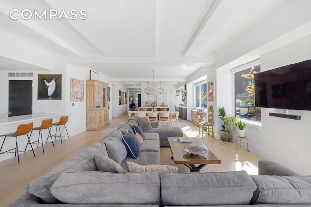 living room featuring beamed ceiling, a chandelier, and light hardwood / wood-style floors