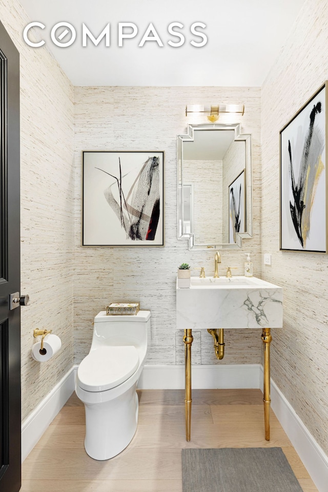 half bath with toilet, wood finished floors, and baseboards