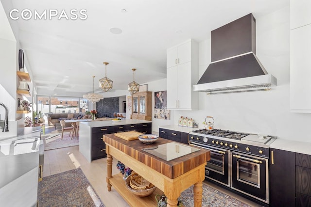 kitchen with a kitchen island, pendant lighting, white cabinets, range with two ovens, and wall chimney range hood