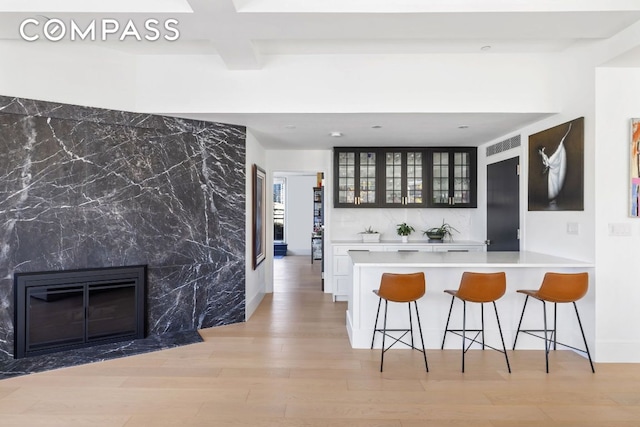 kitchen featuring a breakfast bar area, beam ceiling, light hardwood / wood-style flooring, kitchen peninsula, and a fireplace