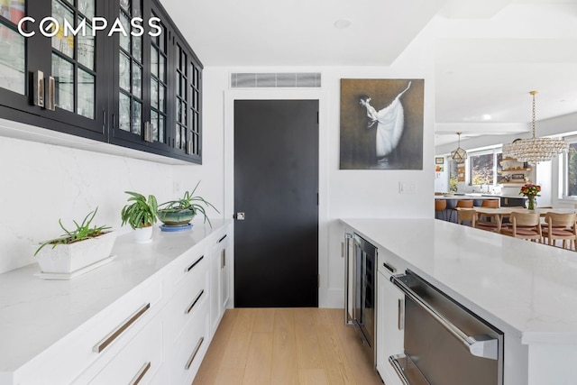 kitchen with hanging light fixtures, light stone countertops, white cabinets, beverage cooler, and light wood-type flooring