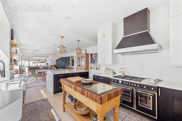 kitchen featuring a kitchen island, decorative light fixtures, range with two ovens, white cabinetry, and wall chimney exhaust hood