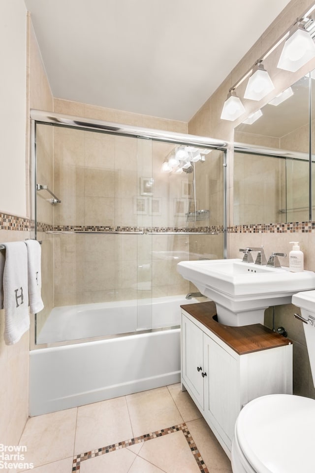 bathroom with tile patterned flooring, tile walls, toilet, and bath / shower combo with glass door