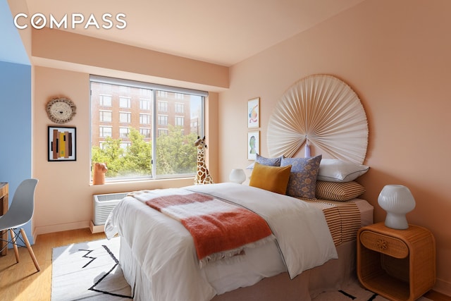 bedroom featuring a wall unit AC, baseboards, and wood finished floors