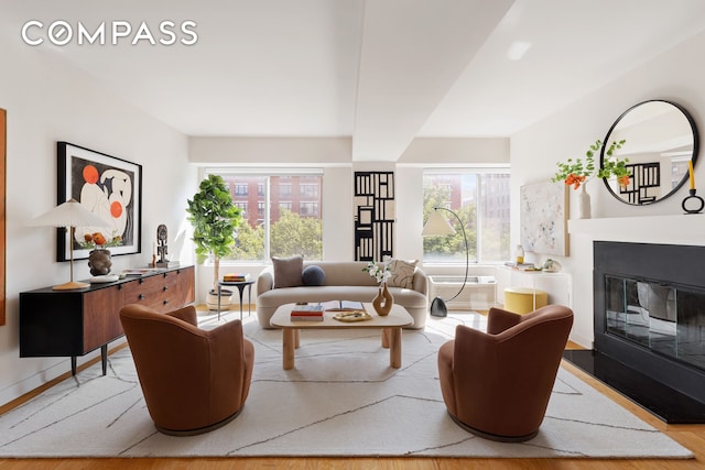 living area featuring a wall mounted air conditioner, wood finished floors, and a glass covered fireplace