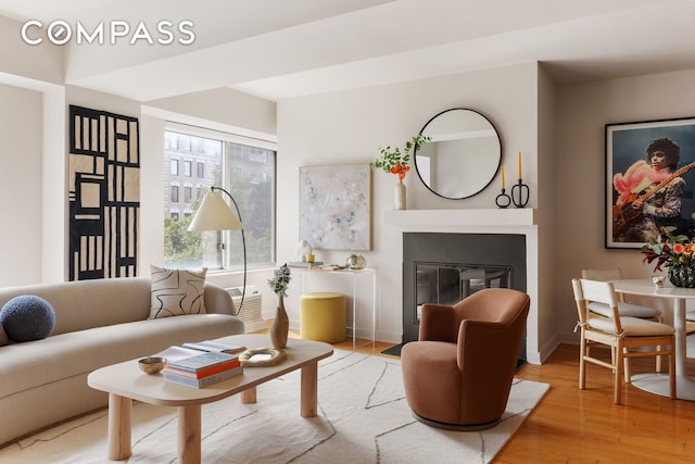 living area with light wood-type flooring, baseboards, and a glass covered fireplace