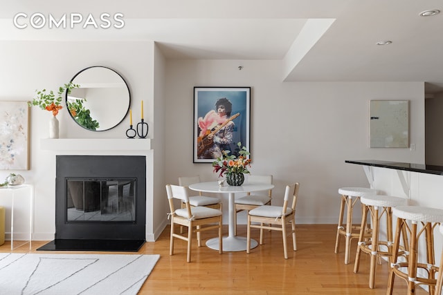 dining space with baseboards, light wood-style floors, and a glass covered fireplace