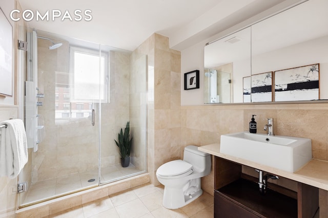 bathroom with tile patterned floors, a stall shower, toilet, and tile walls