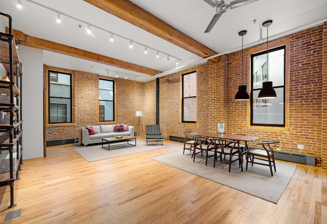 dining space with a healthy amount of sunlight, beamed ceiling, brick wall, and wood finished floors