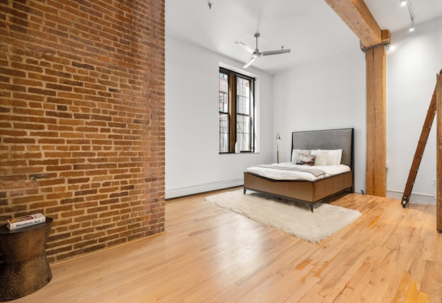 bedroom with decorative columns, a baseboard radiator, brick wall, light wood-type flooring, and beamed ceiling