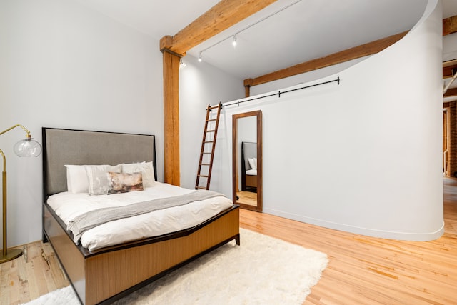 bedroom featuring wood finished floors, baseboards, beamed ceiling, ensuite bath, and track lighting